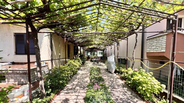 Een overdekte doorgang met een pergola, omringd door plantenbakken en een pad van bakstenen.
