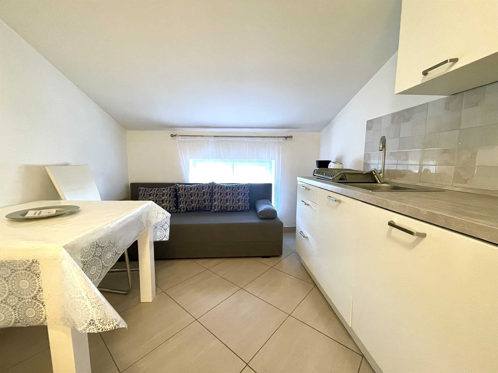 A compact kitchen with a dining table, a sofa, and a window with curtains.