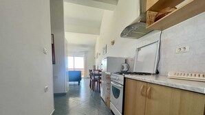 Een keuken met een fornuis, oven en magnetron. Er is een eethoek met stoelen en een tafel.