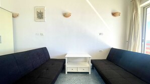 Een kamer met twee donkere banken, een witte bijzettafel en een ingelijst schilderij aan de muur.
