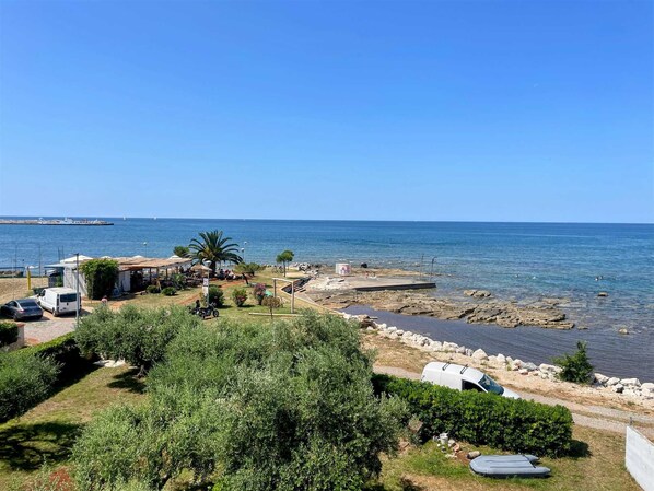 A coastal area with a rocky beach, parked vehicles, and a clear view of the sea. - Apartment Sea View 1 first row to the sea (Umag)
