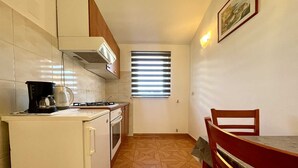Uma cozinha compacta com fogão, cafeteira e um espaço de refeições com uma cadeira.