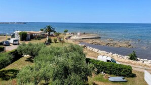 Uma área costeira com uma praia de pedras, veículos estacionados e uma vista clara do mar.