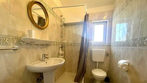 Casa de banho com lavatório suspenso, sanita, chuveiro e janela.