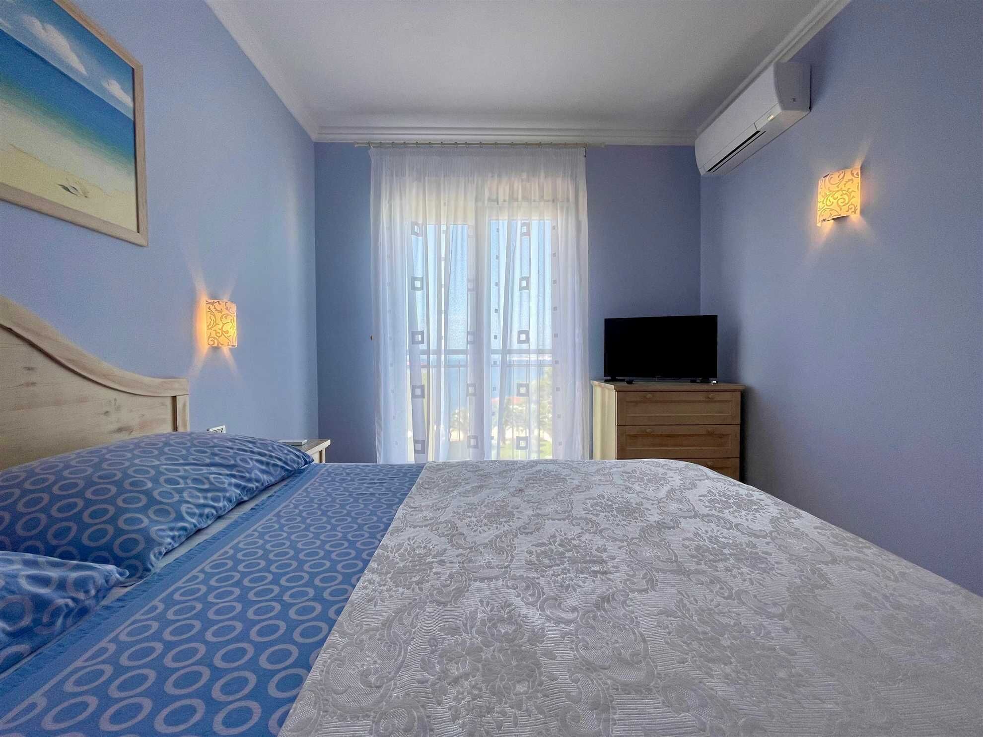 A bedroom with a bed, a TV, a dresser, and a window with curtains.