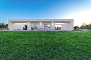 Uma casa moderna com telhado plano, um gramado amplo e um espaço de varanda com móveis de exterior.