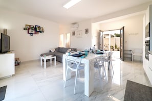 Uma sala de estar moderna com sofá, mesa de jantar com cadeiras, televisão e um objeto decorativo na parede.