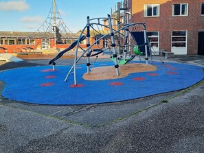 Ein Spielplatz mit Klettergerüst und Rutschen, umgeben von einer blauen, gummierten Fläche.