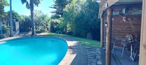 A swimming pool with a stone border, surrounded by lush greenery and a wooden deck.