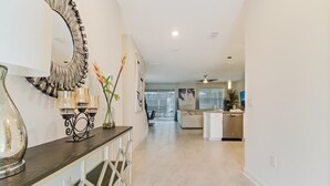A modern kitchen with white appliances, a dining area with a dark wooden table and white chairs, and a hallway leading to a living area.