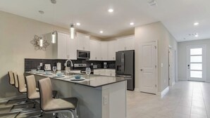 A modern kitchen with a central island, stainless steel appliances, and a dining area with chairs.