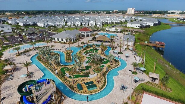 An aerial view of a resort with a large swimming pool, a water slide, and a golf course.