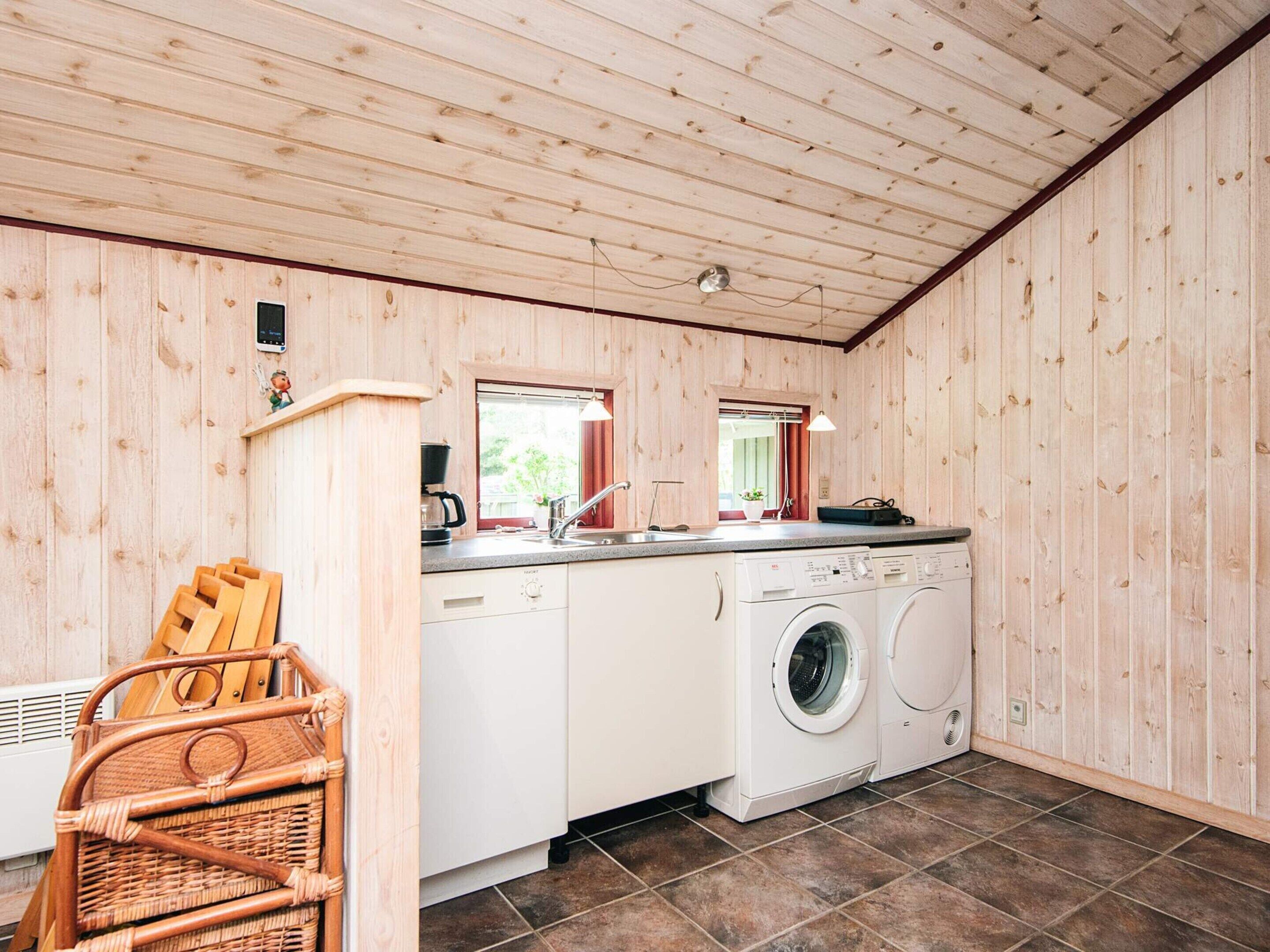 Een compacte keuken met houten wanden, een wasmachine, een spoelbak en een klein raam.
