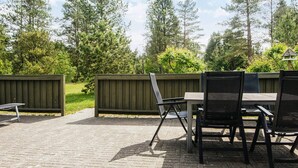 An outdoor patio area with a table and chairs, surrounded by a wooden fence and trees. - 8 Person Holiday Home in Norre Nebel (Norre Nebel)