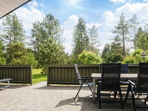 An outdoor patio area with a table and chairs, surrounded by a wooden fence and trees. - 8 Person Holiday Home in Norre Nebel (Norre Nebel)