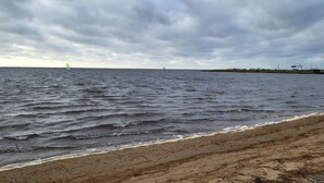 A beach with waves, a distant sailboat, and a cloudy sky. - 8 Person Holiday Home in Norre Nebel (Norre Nebel)