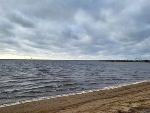 A beach with waves, a distant sailboat, and a cloudy sky. - 8 Person Holiday Home in Norre Nebel (Norre Nebel)