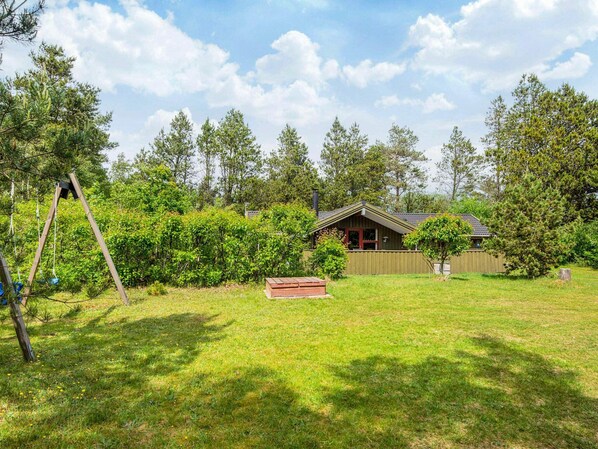 A wooden cabin with a fenced yard, surrounded by trees and a swing set.