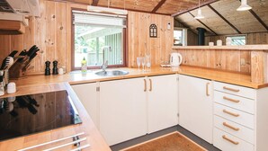 A modern kitchen with wooden cabinets, a black countertop, and a window with blinds. - 8 Person Holiday Home in Norre Nebel (Norre Nebel)