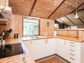 A modern kitchen with wooden cabinets, a black countertop, and a window with blinds. - 8 Person Holiday Home in Norre Nebel (Norre Nebel)
