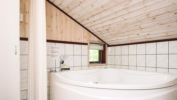A modern bathroom with a large freestanding bathtub, wooden ceiling, and tiled walls.