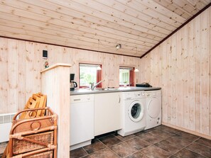 A compact kitchen with wooden walls, a washing machine, and a wicker chair.