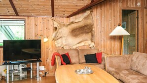 A cozy living room with a wooden ceiling, a mounted television, a sofa, and a dining table.