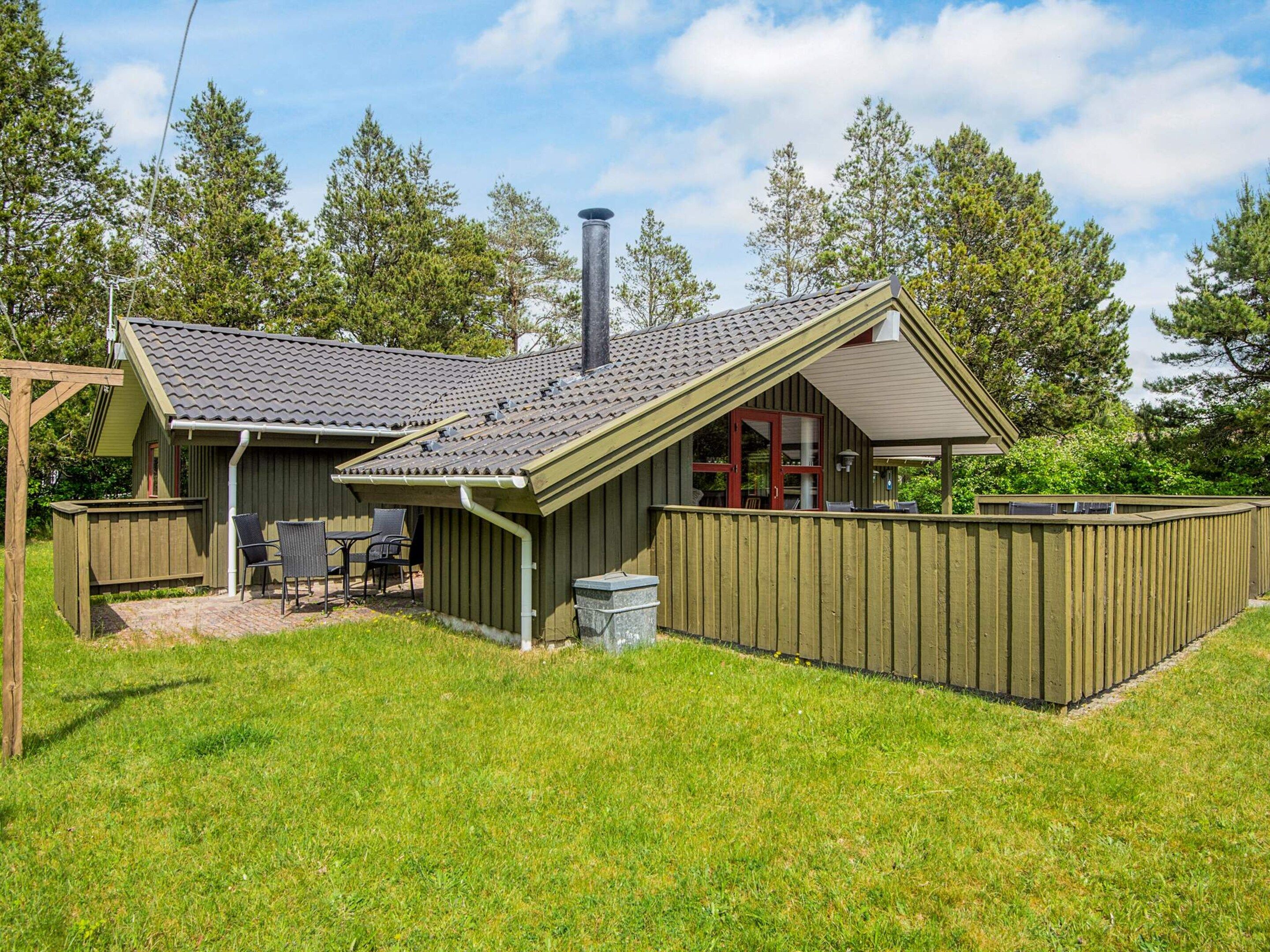 A wooden cabin with a sloped roof, a fenced backyard, and a chimney.