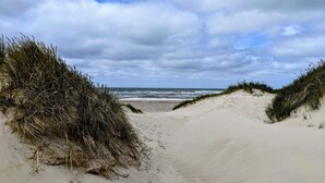 A sandy beach with dunes and a cloudy sky.