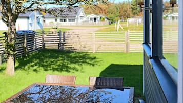 A patio with wicker furniture and a glass table, overlooking a grassy area with a wooden fence and houses in the background.