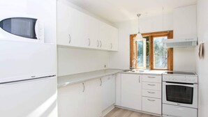 A modern kitchen with white cabinets, a built-in microwave, a sink, and a stove. - 6 Person Holiday Home in Nexo (Nexø)