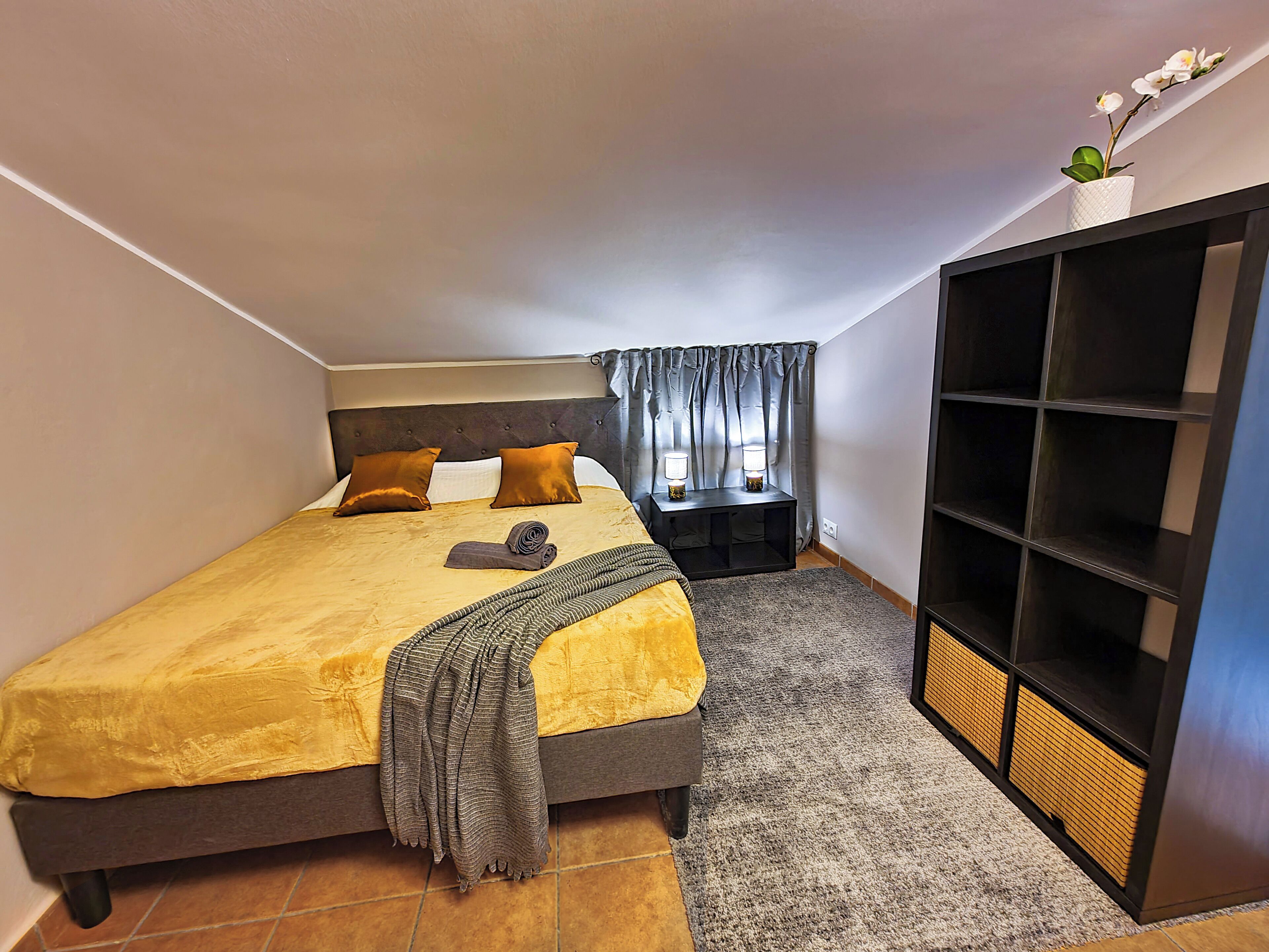 Ein Schlafzimmer mit Bett, Nachttisch, Kleiderschrank und einem Fenster mit Vorhängen.