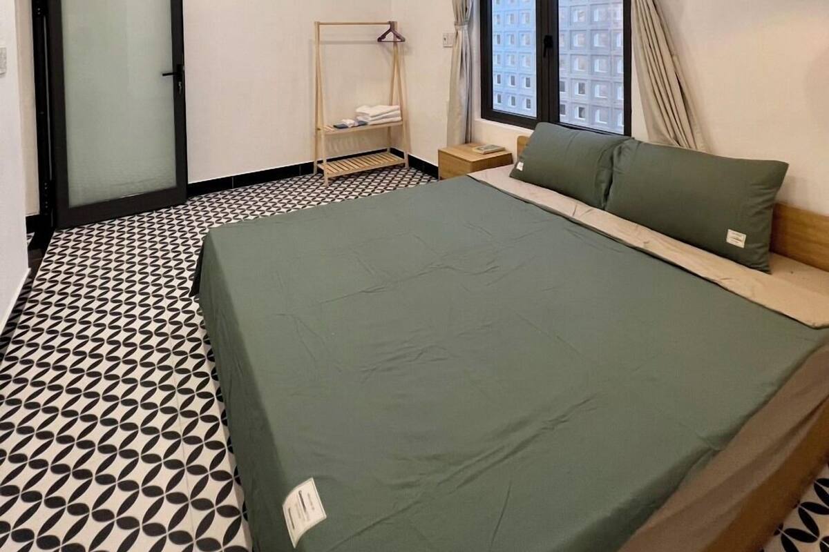 Quarto de hotel com cama, janela com cortinas, luminária pendente e piso de azulejos.