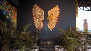 Un área de recepción con una pared decorativa que presenta un motivo de ala dorada y un letrero que dice "#LUCIFER@RC Párate aquí para Fotos".