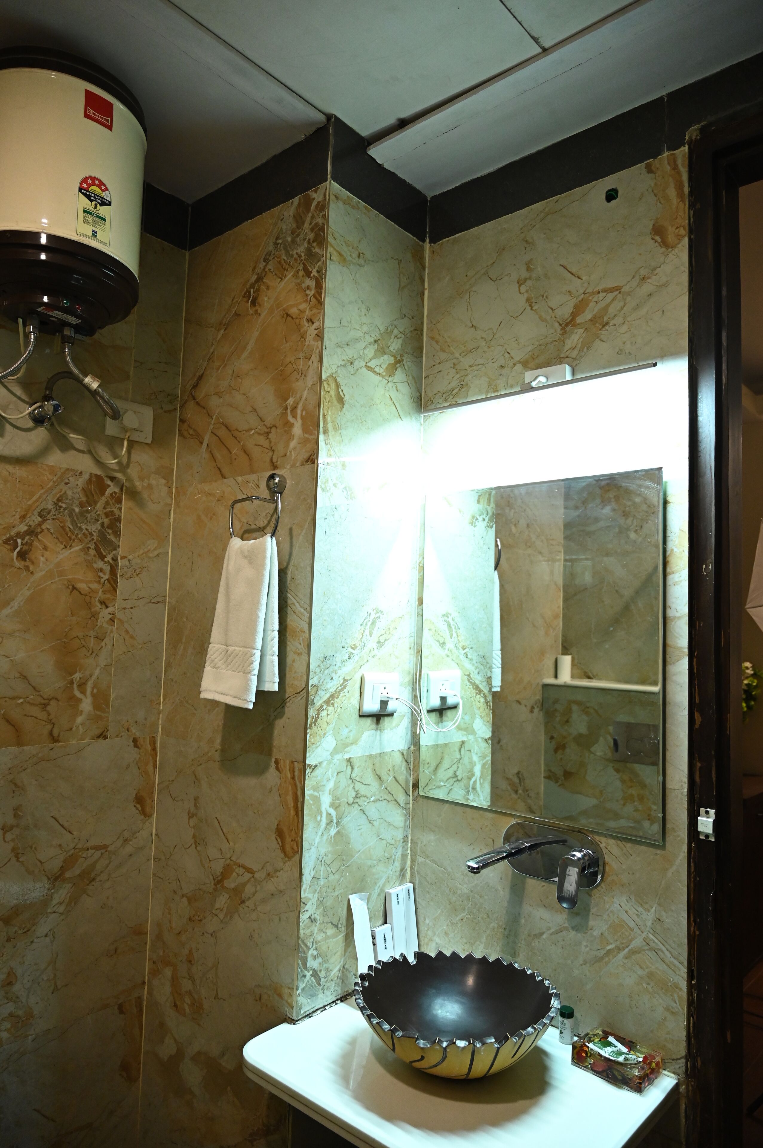 Un baño con pared de mármol, un lavabo con un cuenco decorativo, un perchero, un espejo y un cabezal de ducha.