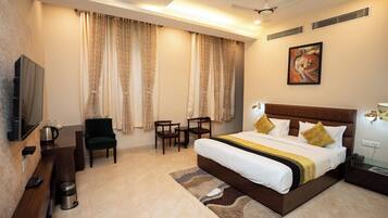 A hotel room with a large bed, a TV, a desk, and a chair.