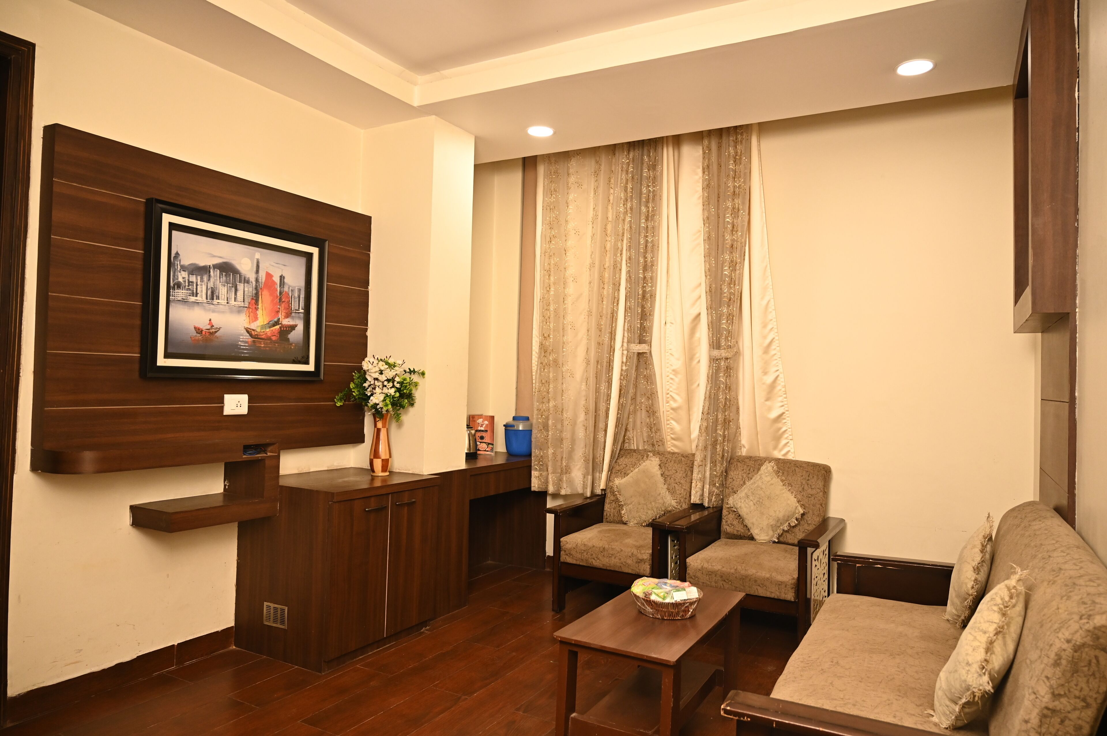 A living room with a sofa set, a coffee table, a TV mounted on the wall, and a decorative plant.