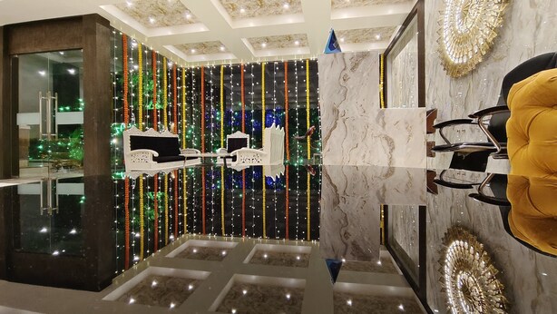 Un moderno vestíbulo de hotel con piso reflectante, una zona de estar con sofá blanco y una pared decorativa con motivo circular.