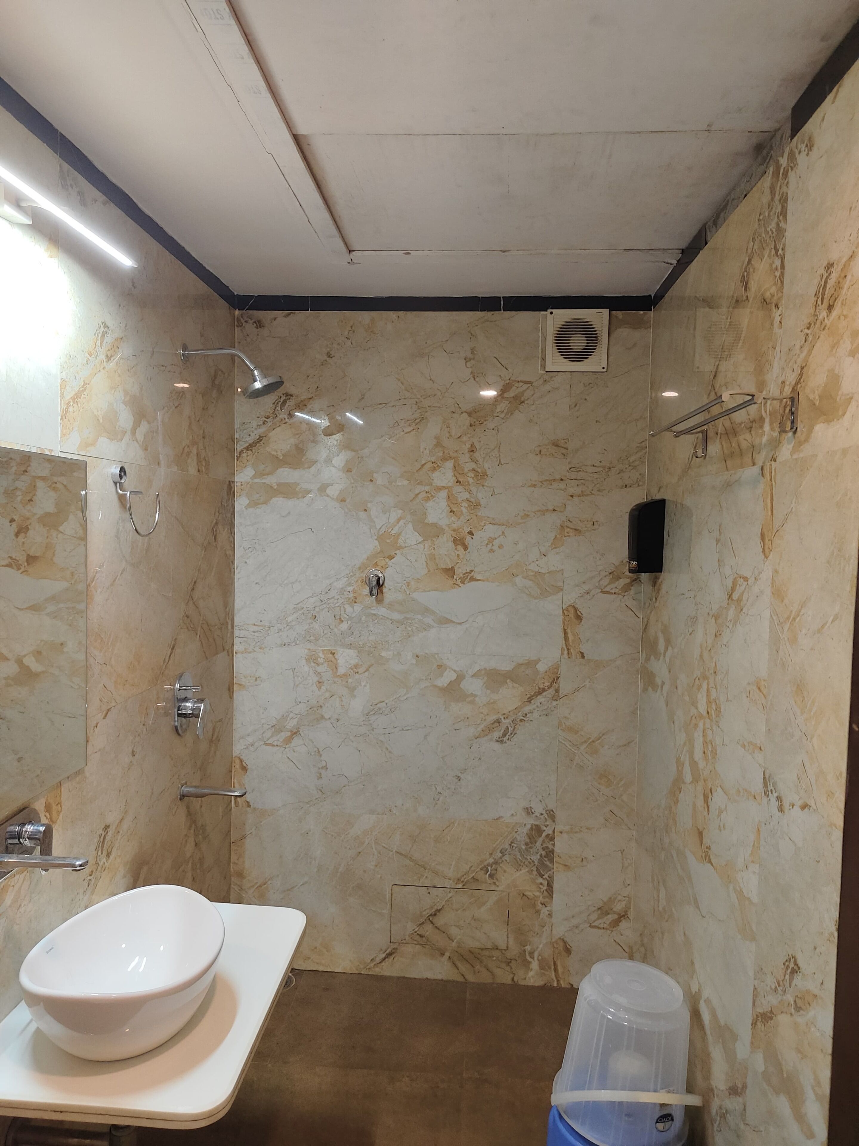 Un baño con pared de mármol, un lavamanos blanco, ducha y toallero.
