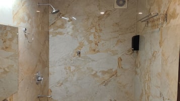 Un baño con pared de mármol, un lavamanos blanco, ducha y toallero.