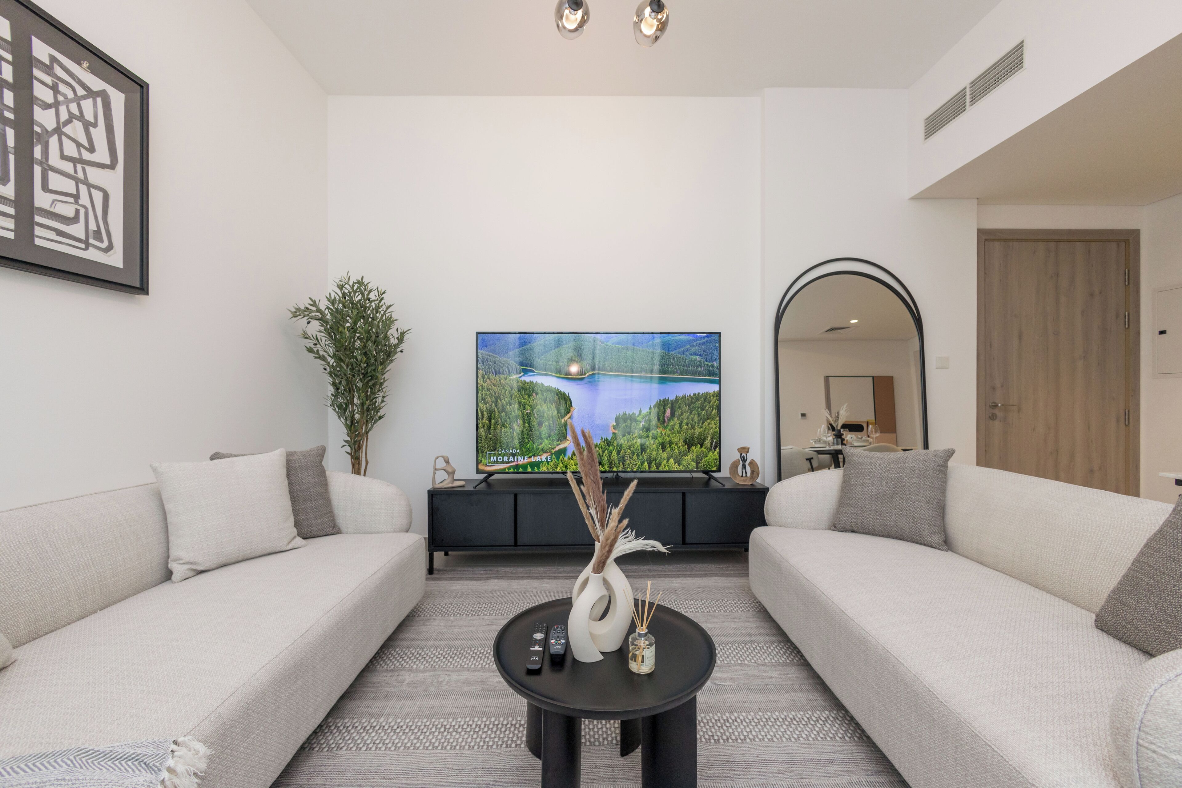 Ein modernes Wohnzimmer mit einem großen Flachbildfernseher, zwei Sofas, einem Couchtisch und einer dekorativen Vase.