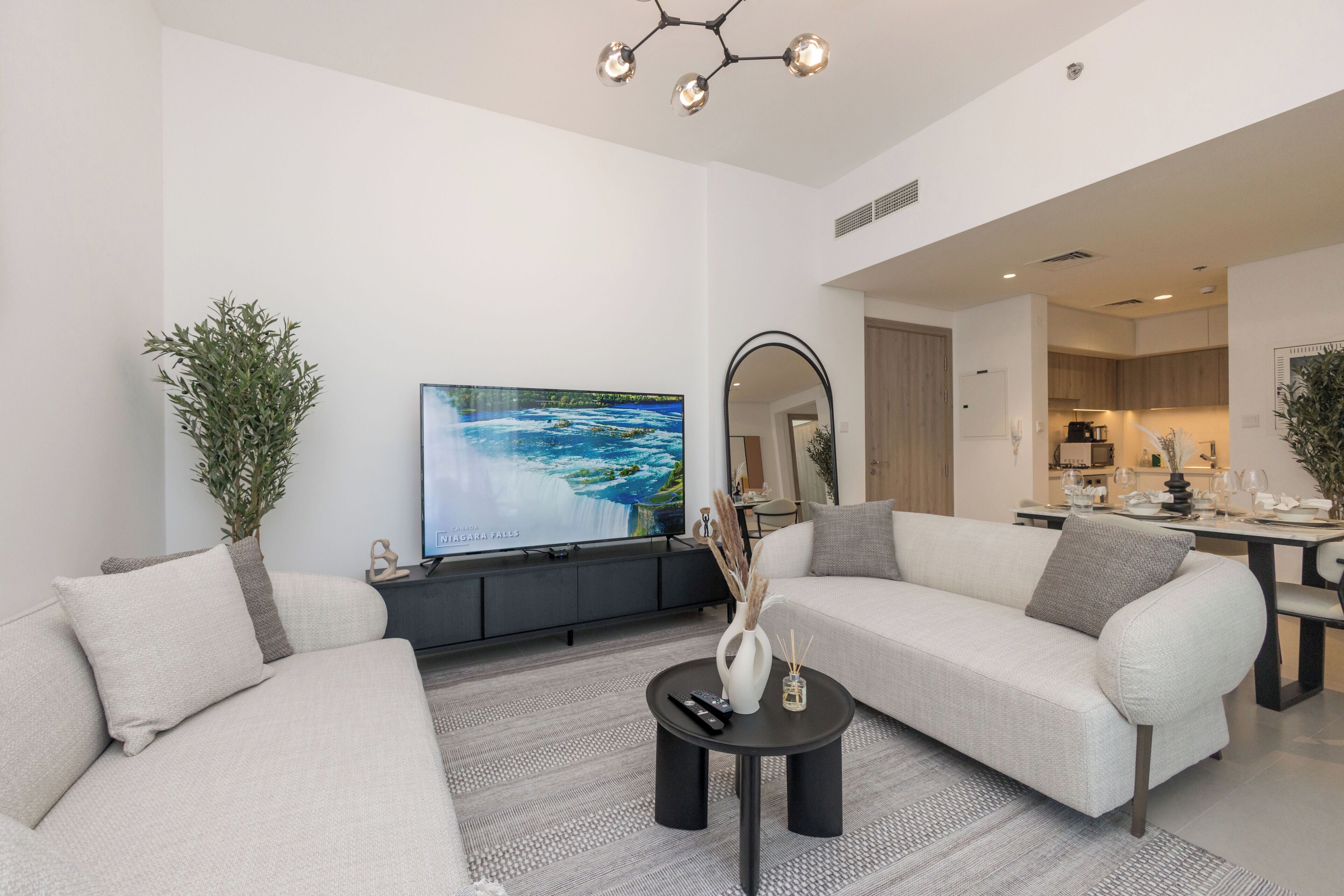 A modern living room with a sofa set, a TV, a coffee table, and a dining area in the background.