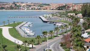 A marina with boats docked, a curved road, and a coastal town in the background. - Holiday Home in Olbia Near Marinella Beach (Golfo Aranci)