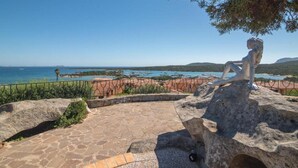 A stone pathway leading to a seating area with a sculpture, overlooking a coastal landscape with clear skies. - Holiday Home in Olbia Near Marinella Beach (Golfo Aranci)