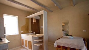 A compact kitchen with a built-in sink, wooden cabinets, and a dining area with a table and chairs. - Holiday Home in Olbia Near Marinella Beach (Golfo Aranci)