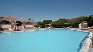 A clear blue swimming pool with lounge chairs and umbrellas, surrounded by stone buildings and greenery. - Holiday Home in Olbia Near Marinella Beach (Golfo Aranci)