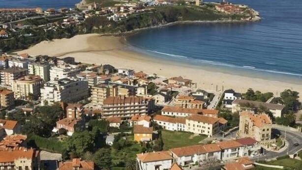 Un pueblo costero con una mezcla de edificios residenciales e históricos, una playa y una estructura fortificada en una colina.