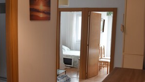 Una habitación con una puerta de madera que da a un dormitorio con una cama, una silla y un televisor.