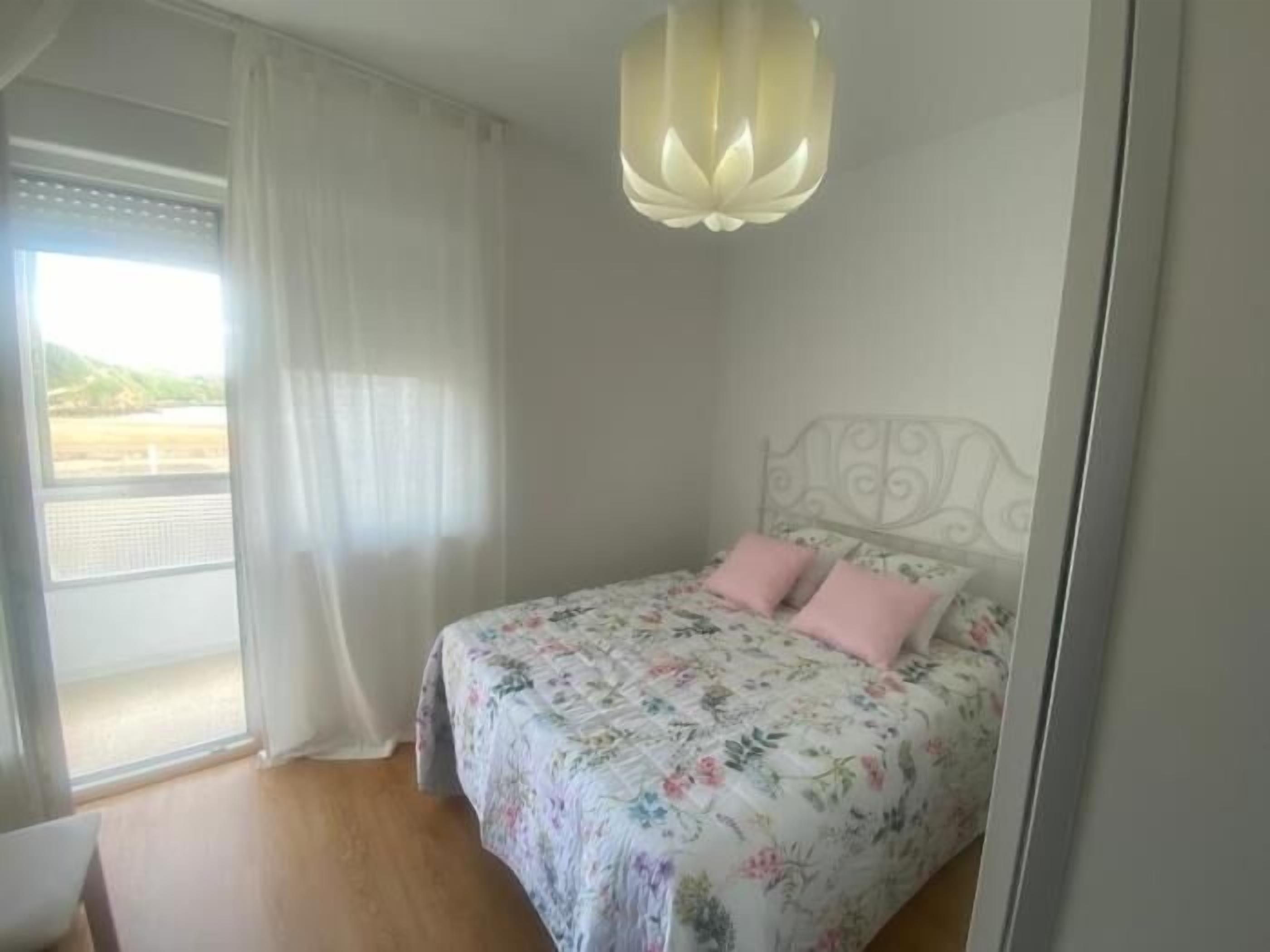 A bedroom with a floral bedspread, a metal headboard, and a view of a body of water through a window.