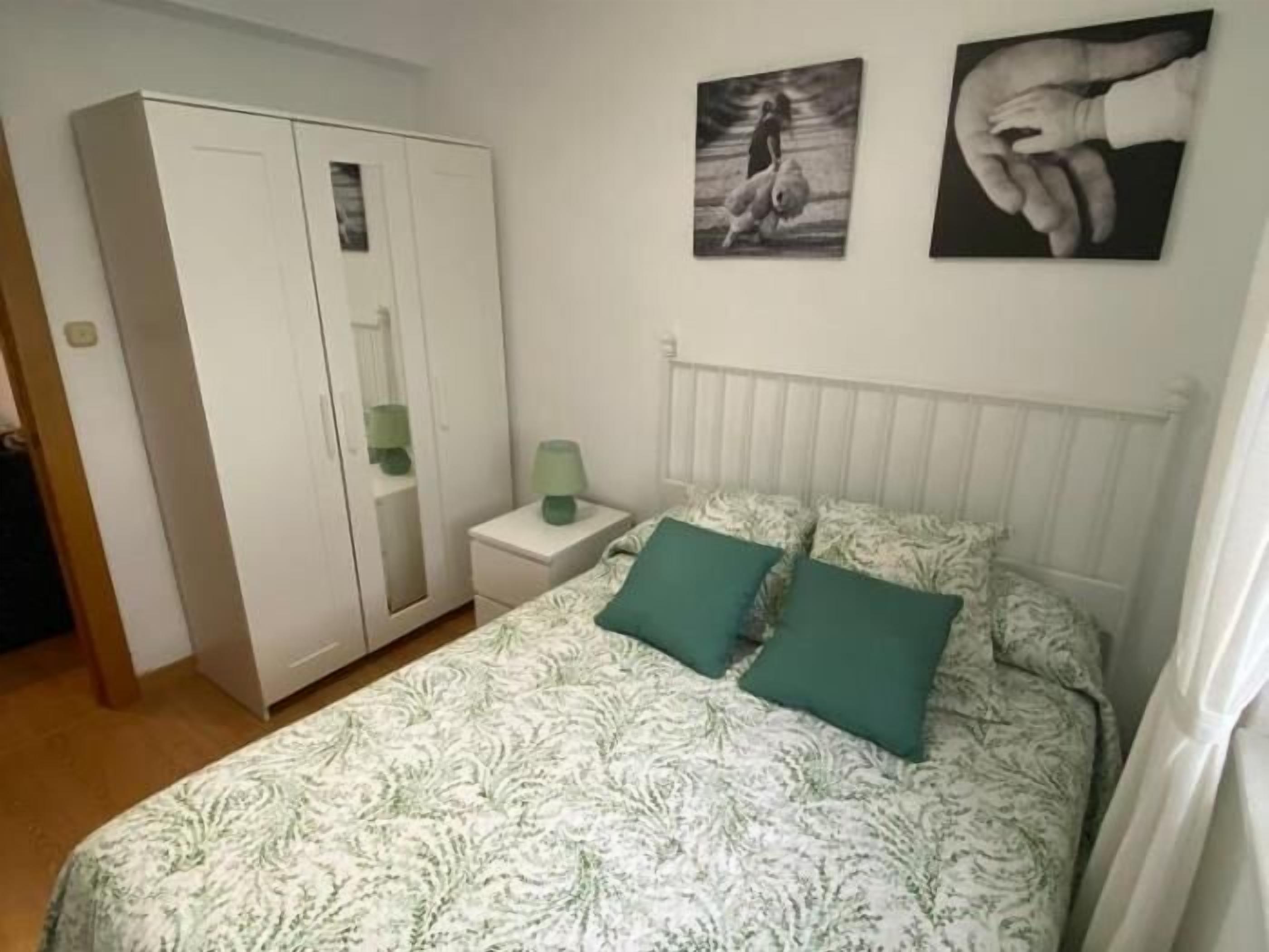 A bedroom with a bed, a wardrobe, a nightstand, and two wall-mounted pictures.